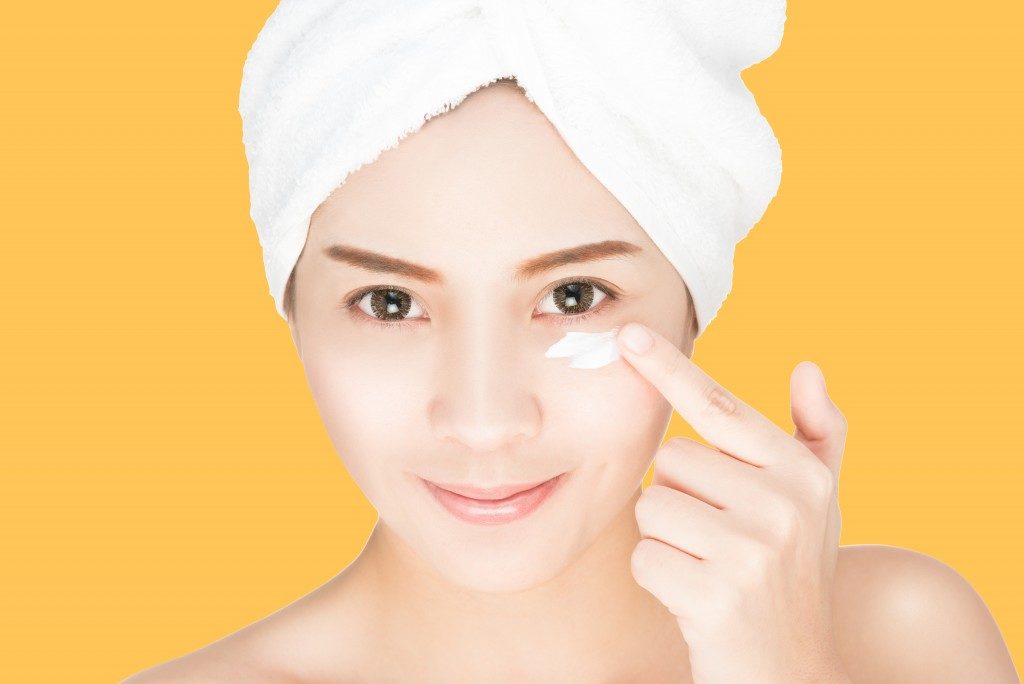 beautiful woman applying skin cream under eyes on her face
