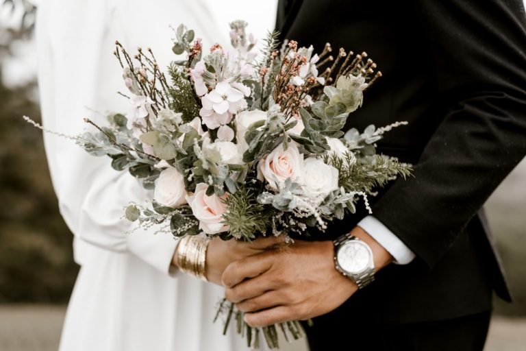 bride and groom standing while holding flowers