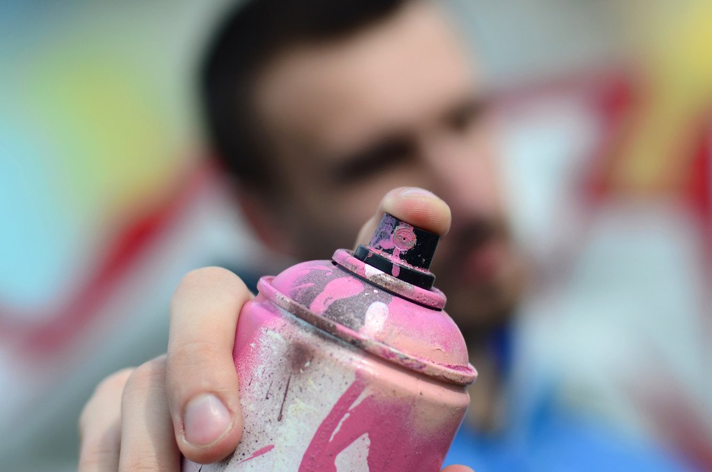 graffiti artist in a blue jacket is holding a can of paint
