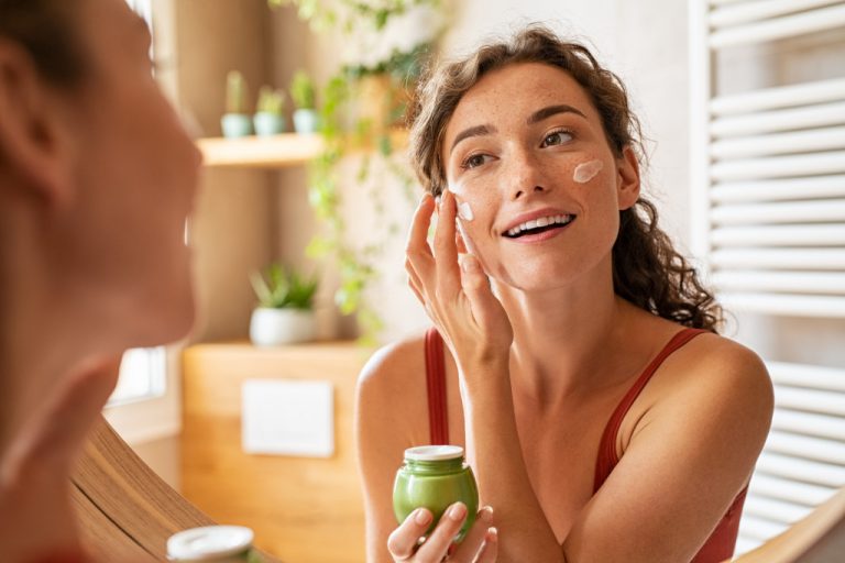 a young woman in front of a mirror applying a beauty cream