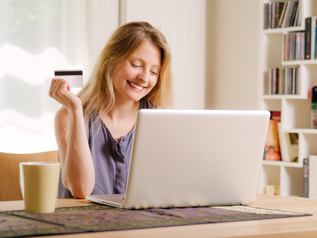 a young woman using a laptop holding a card to shop online