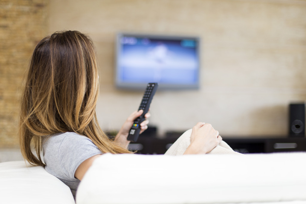 a woman holding a remote while sitting on the couch to watch TV