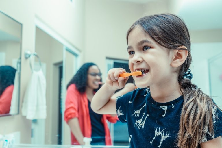 kid brushing her teeth with her parent