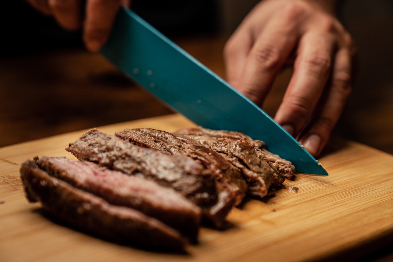 a person slicing steak on a chopping board