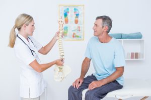 female doctor holding a spine model in front of a senior patient